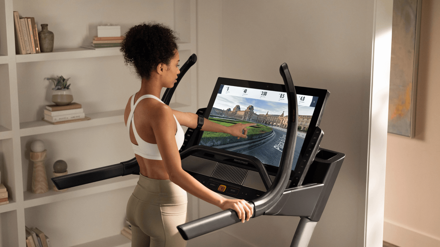 Woman touches her iFIT-enabled treadmill’s screen during a running workout 